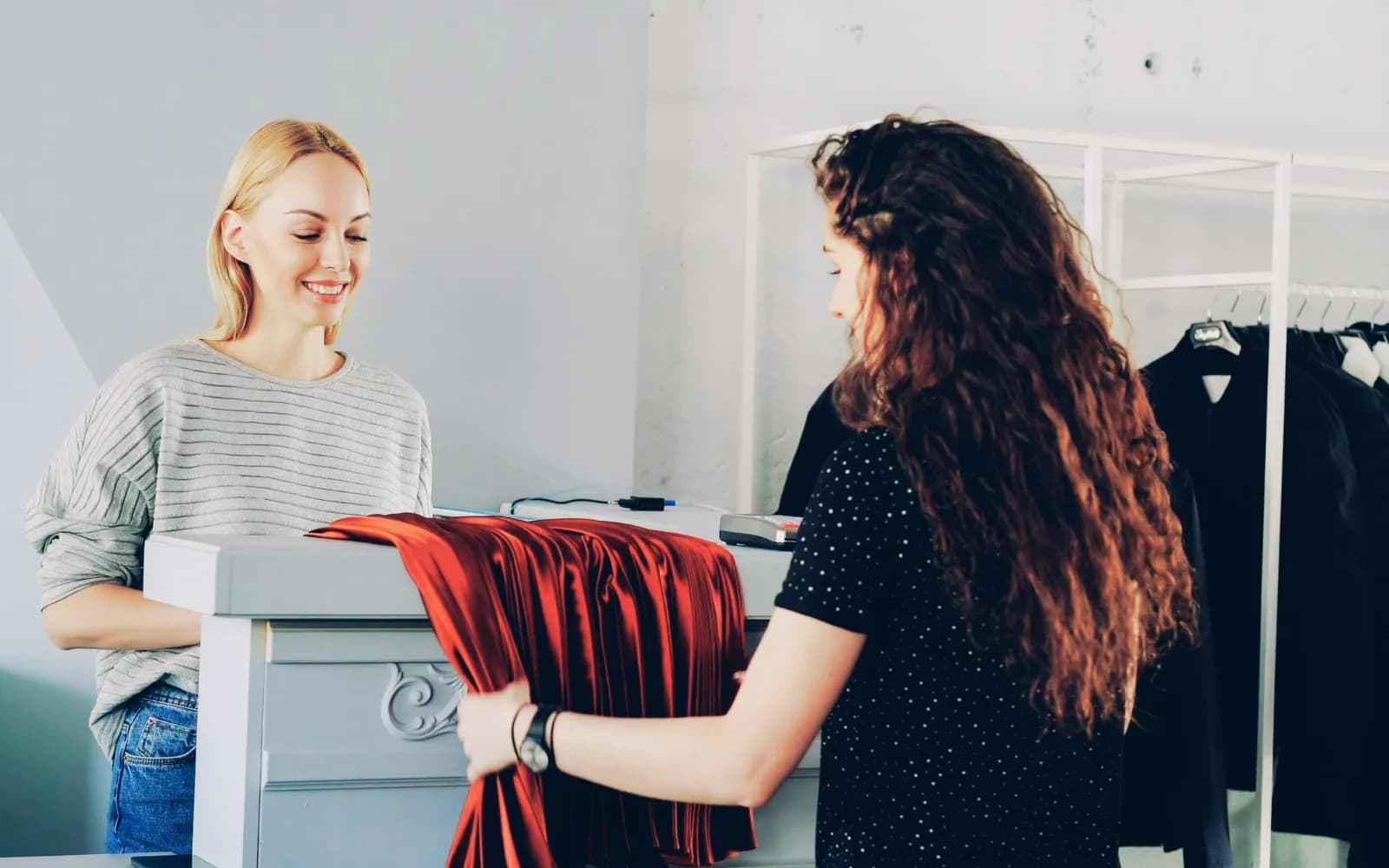 Boutique assistant handing a red garment to a customer across the store counter