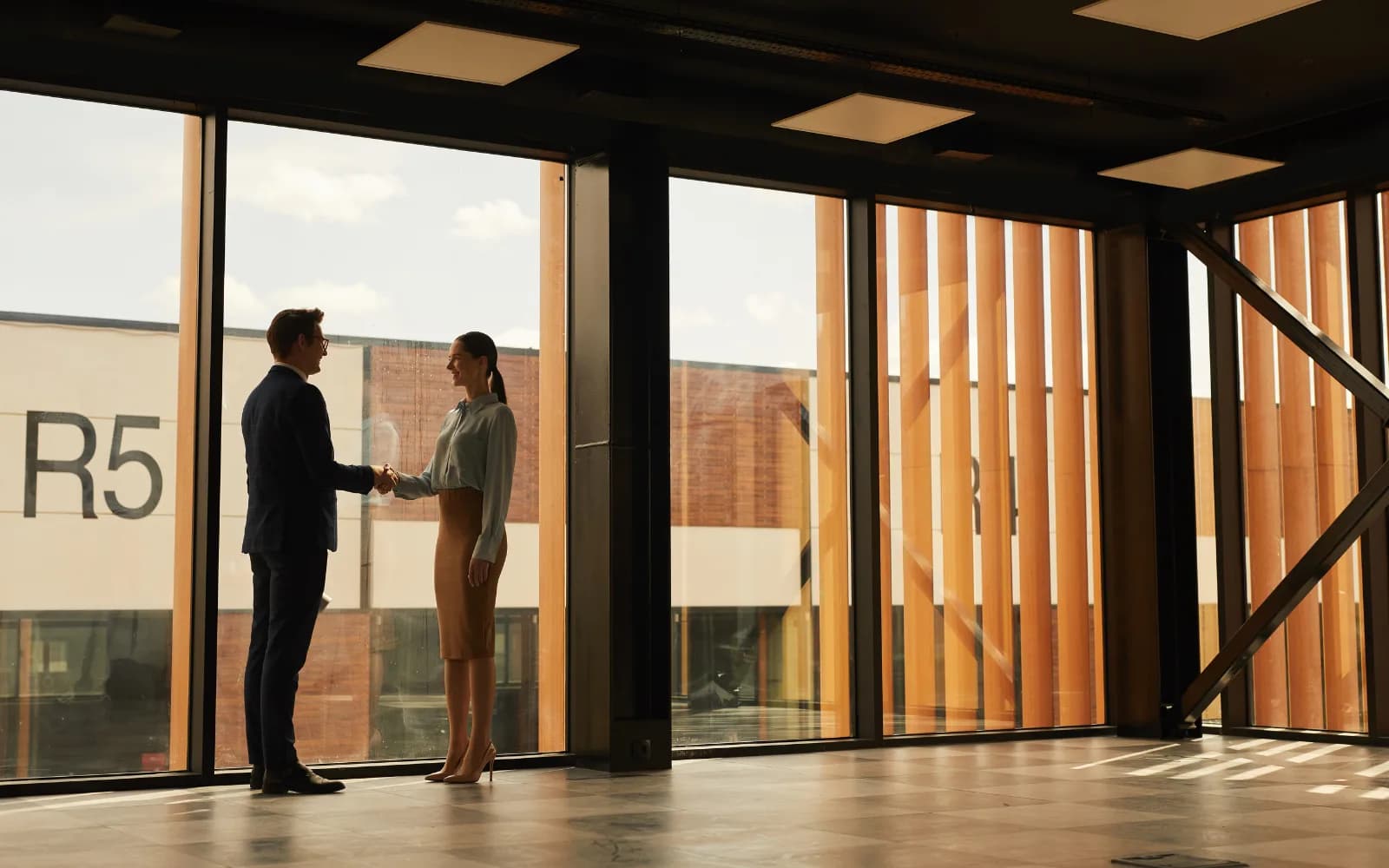 Two professionals shaking hands by the window of a bright, newly built commercial space